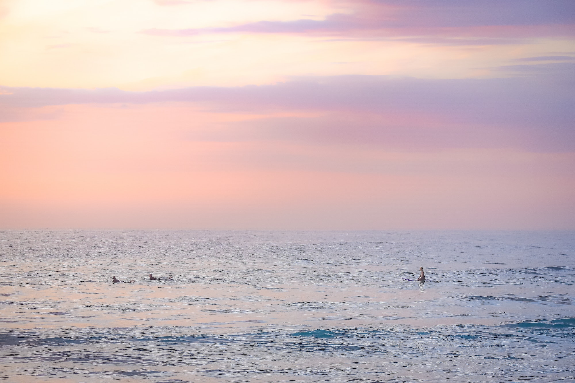 Surfers waiting on the ocean surface at sunrise in calm conditions